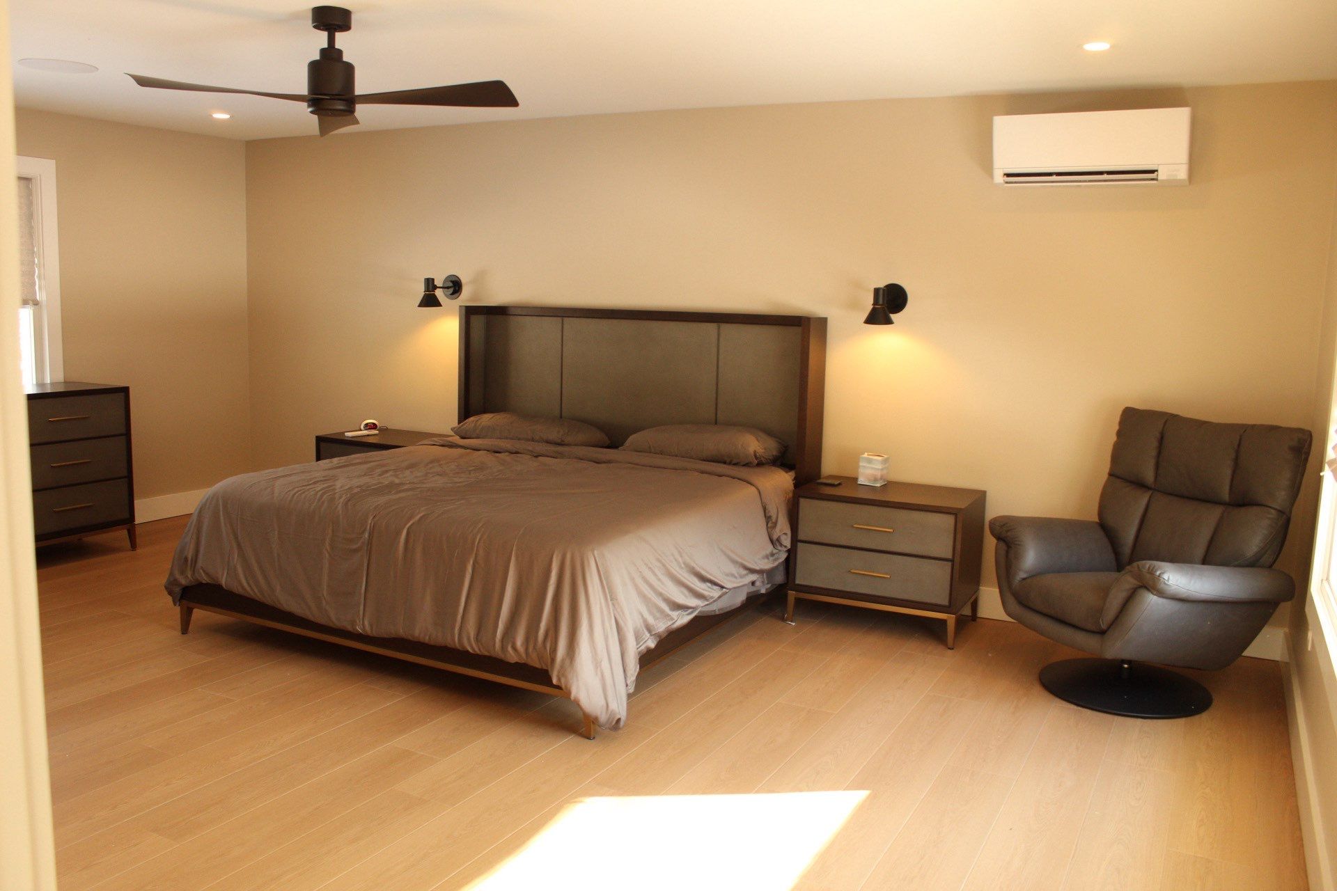 Hotel-style bedroom with a large bed, two nightstands, wall lamps, and a ceiling fan; beige walls and light wood floors.