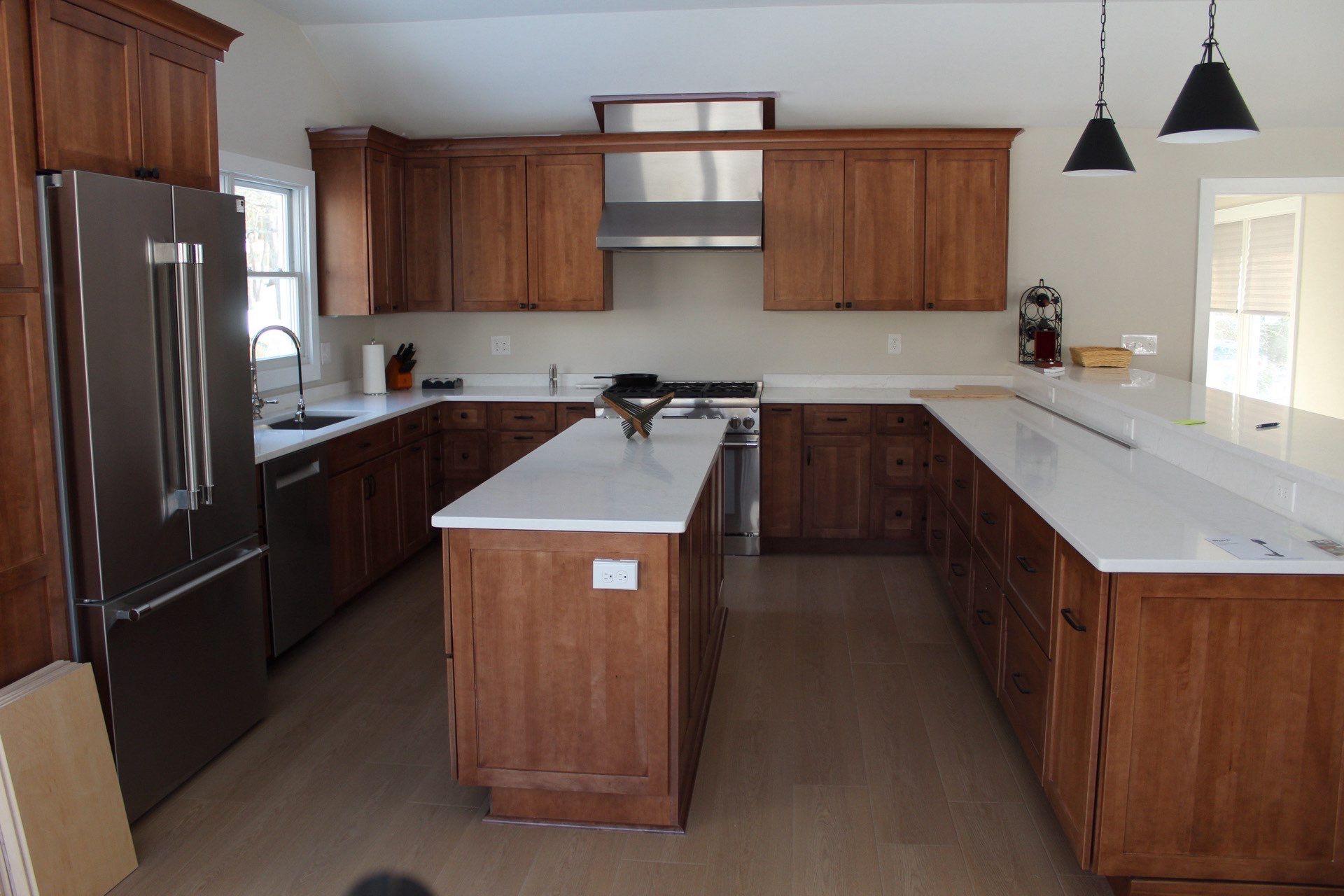 Modern kitchen with wooden cabinets, white countertops, and a stainless steel refrigerator and stove.