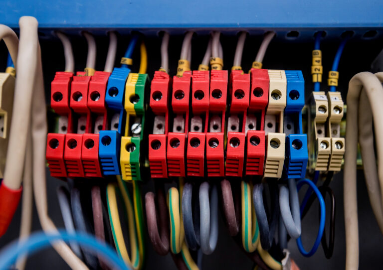 Close-up of colorful modular terminal blocks and cables in a network patch panel, showing red, blue, yellow, green blocks and tagged wires.