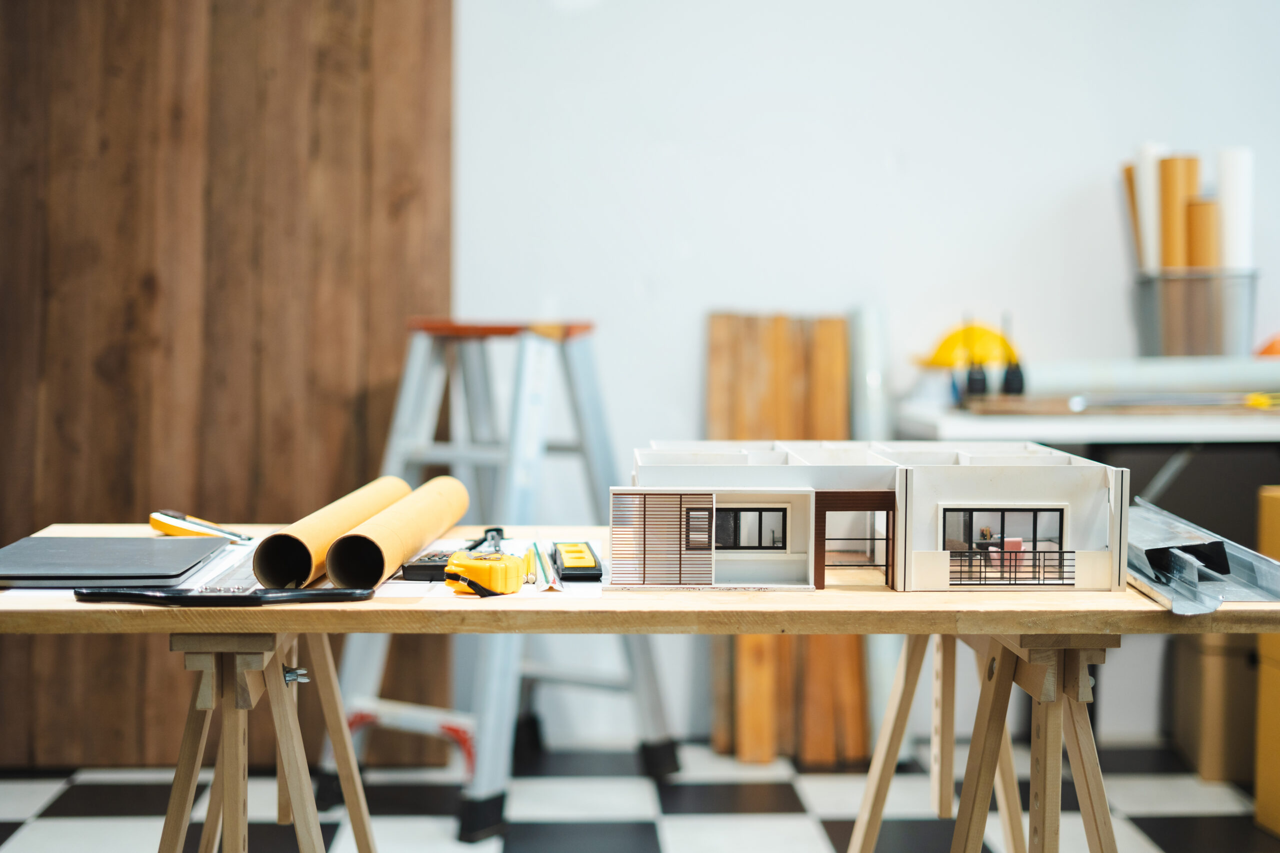 Architectural models and drafting tools spread across a workshop table in a design studio