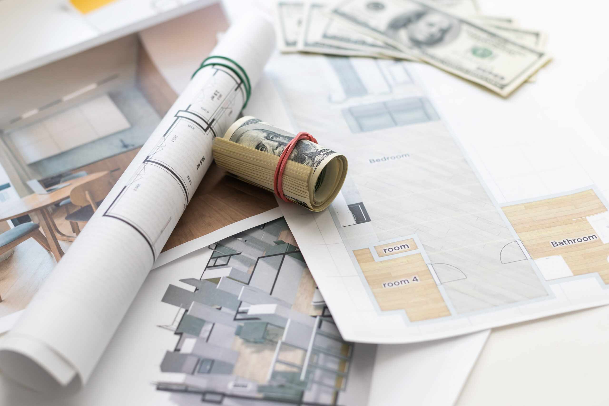 Rolled architectural blueprints with a bundle of cash laid atop floor plans showing labeled rooms like bedroom and bathroom.